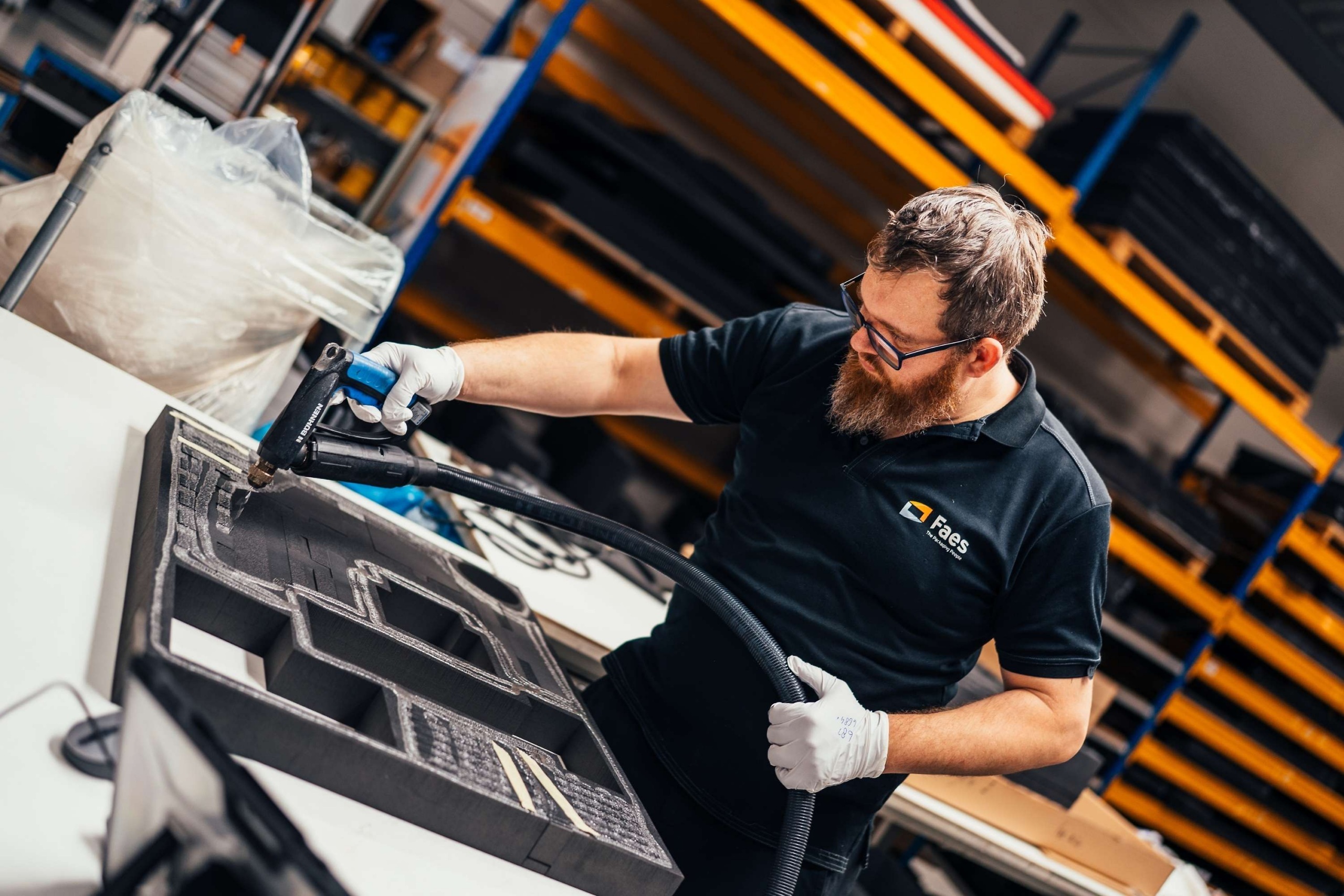 Medewerker van Faes werkt met handschoenen en een handgereedschap aan een zwart foam interieur met maatwerk uitsparingen, passend bij beschermende verpakkingen voor lithium metaal batterijen volgens UN3481-regels.