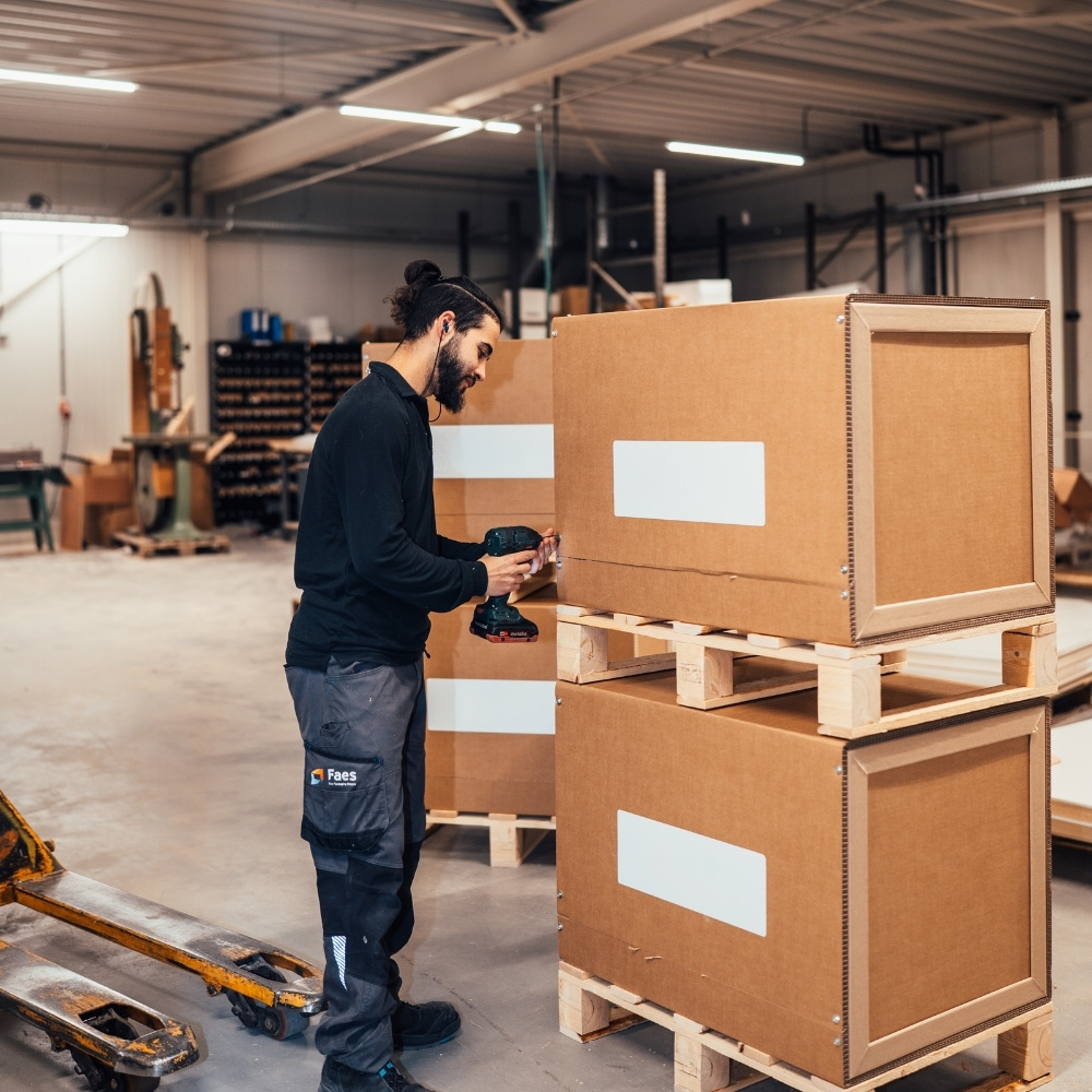 Medewerker van Faes assembleert grote kartonnen palletverpakkingen in de werkplaats, passend bij efficiënte verpakkingsprocessen en TCO-optimalisatie.