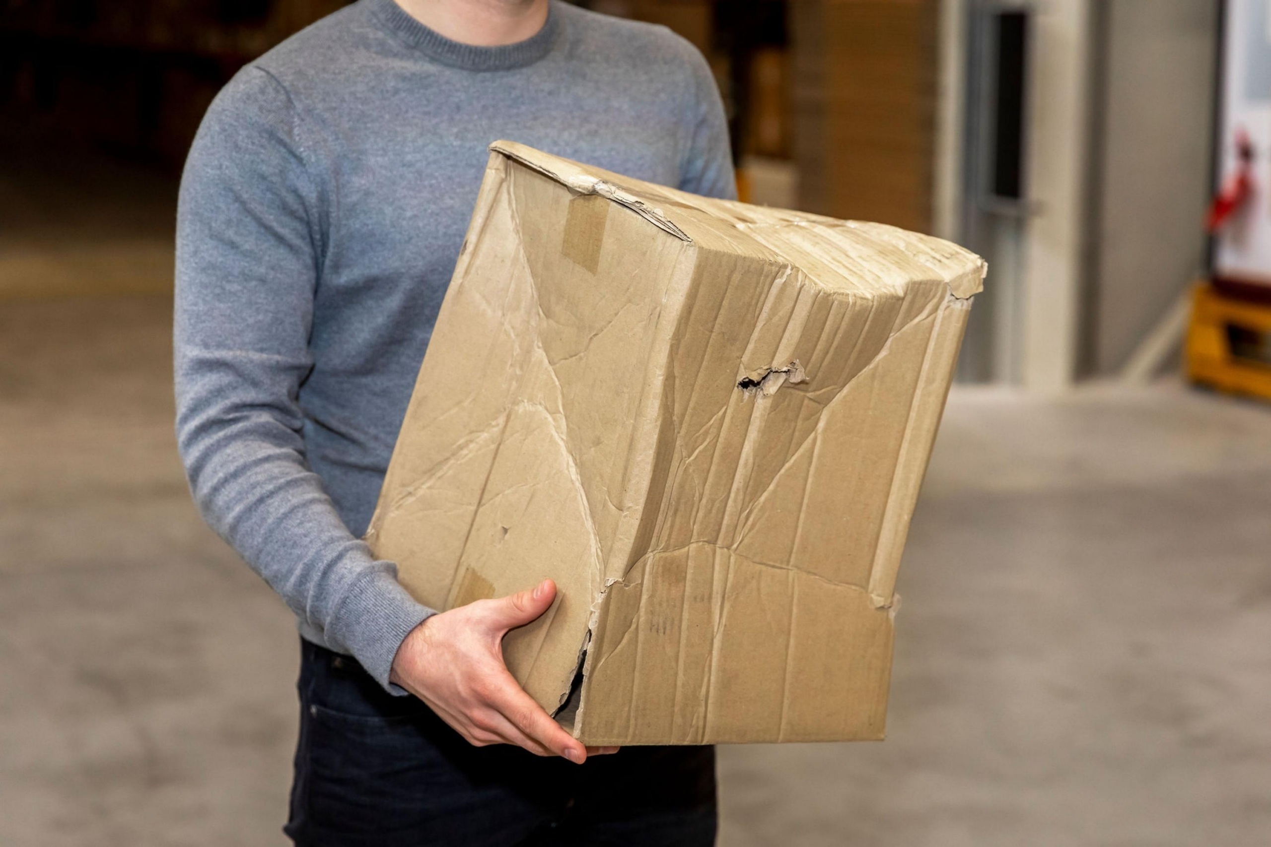 Medewerker van Faes houdt een zichtbaar beschadigde kartonnen verpakking vast, als praktijkvoorbeeld van transportschade die kan leiden tot Dead on Arrival.