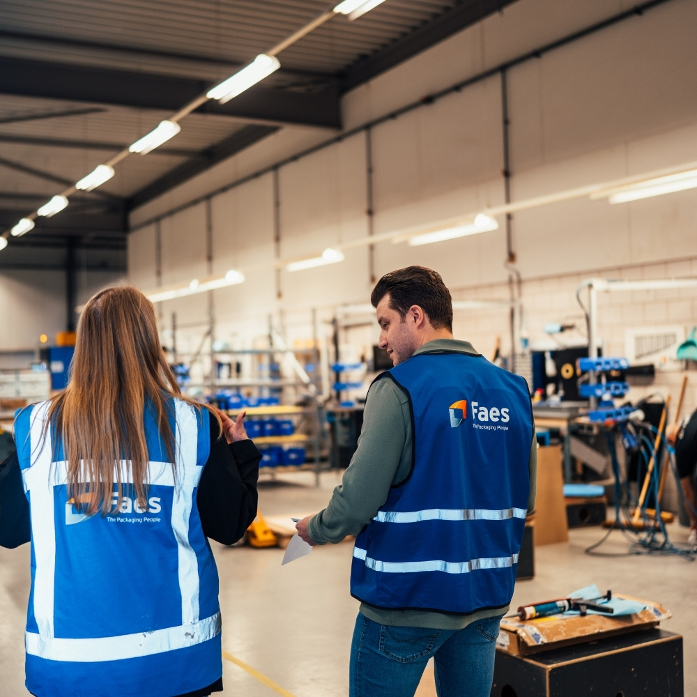 Twee medewerkers van Faes bespreken het werkproces tijdens een rondgang door de productiehal, passend bij gecontroleerde verpakkingsprocessen en effectieve DOA-preventie.