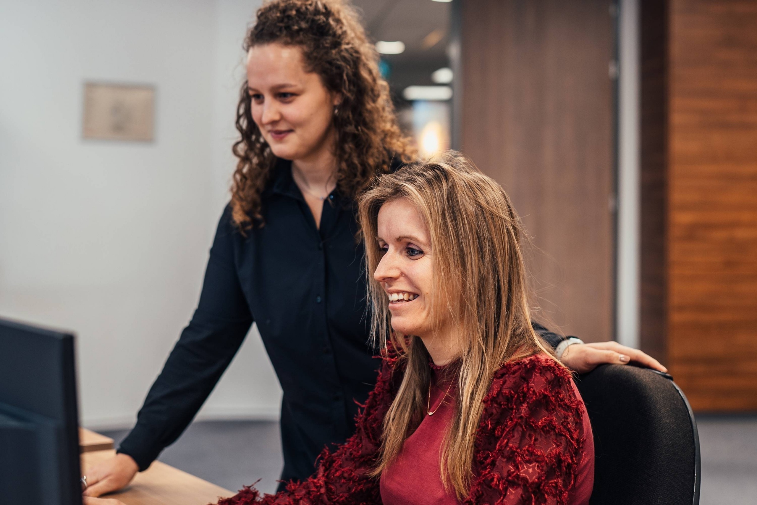 Twee collega’s van Faes werken samen achter een computer in een kantooromgeving, passend bij een artikel over het zorgvuldig rapporteren van DOA-schade voor verzekeringsclaims.