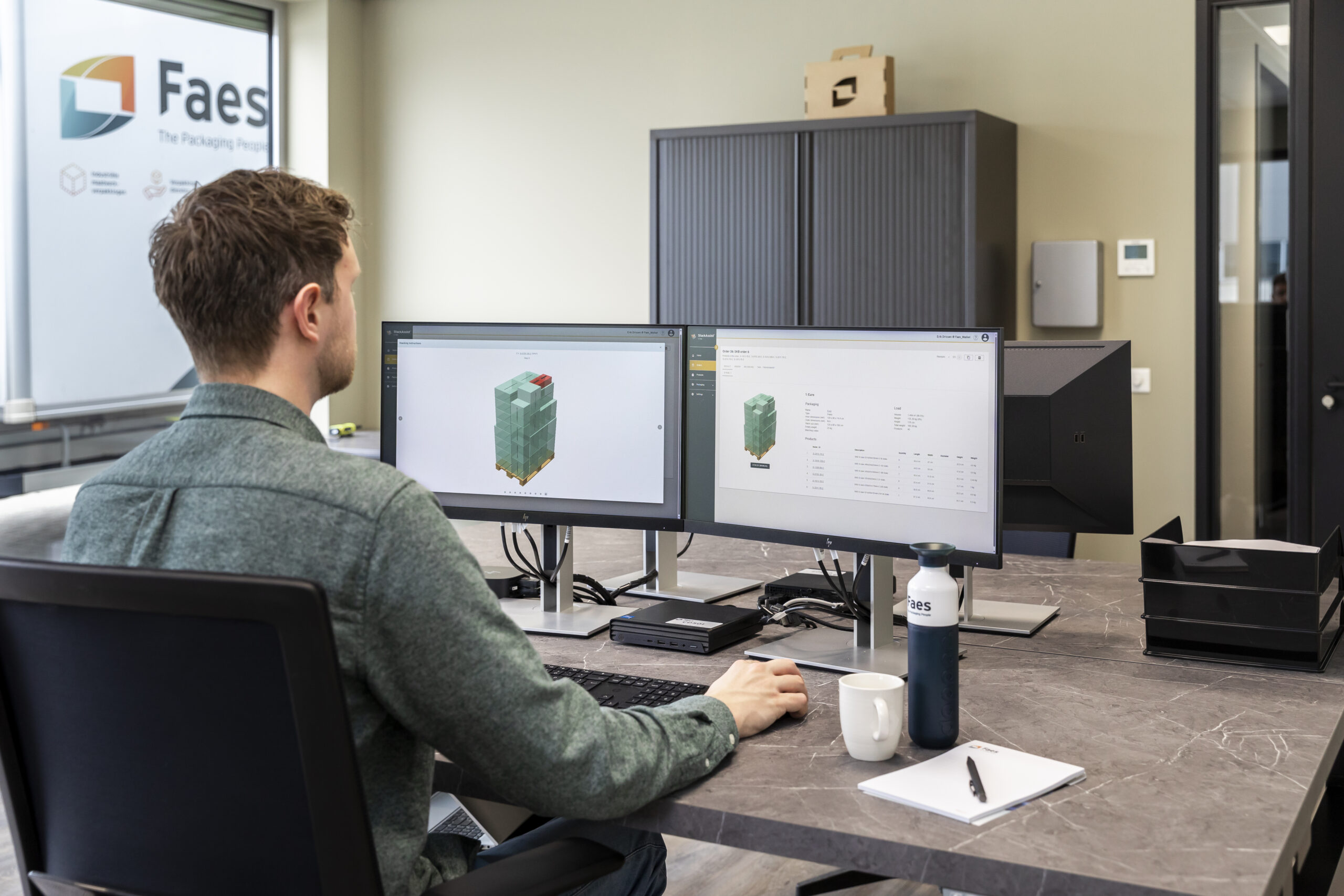 Een medewerker van Faes gebruikt StackAssist-software op dubbele monitoren om een optimale palletconfiguratie te plannen en efficiëntie te verhogen bij het stapelen en verzenden van goederen.