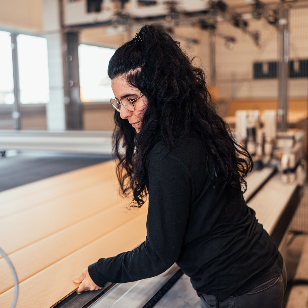 Medewerker van Faes verwerkt een grote kartonnen plaat op een productiemachine, passend bij een efficiënt verpakkingsproces waarin verspilling wordt beperkt.