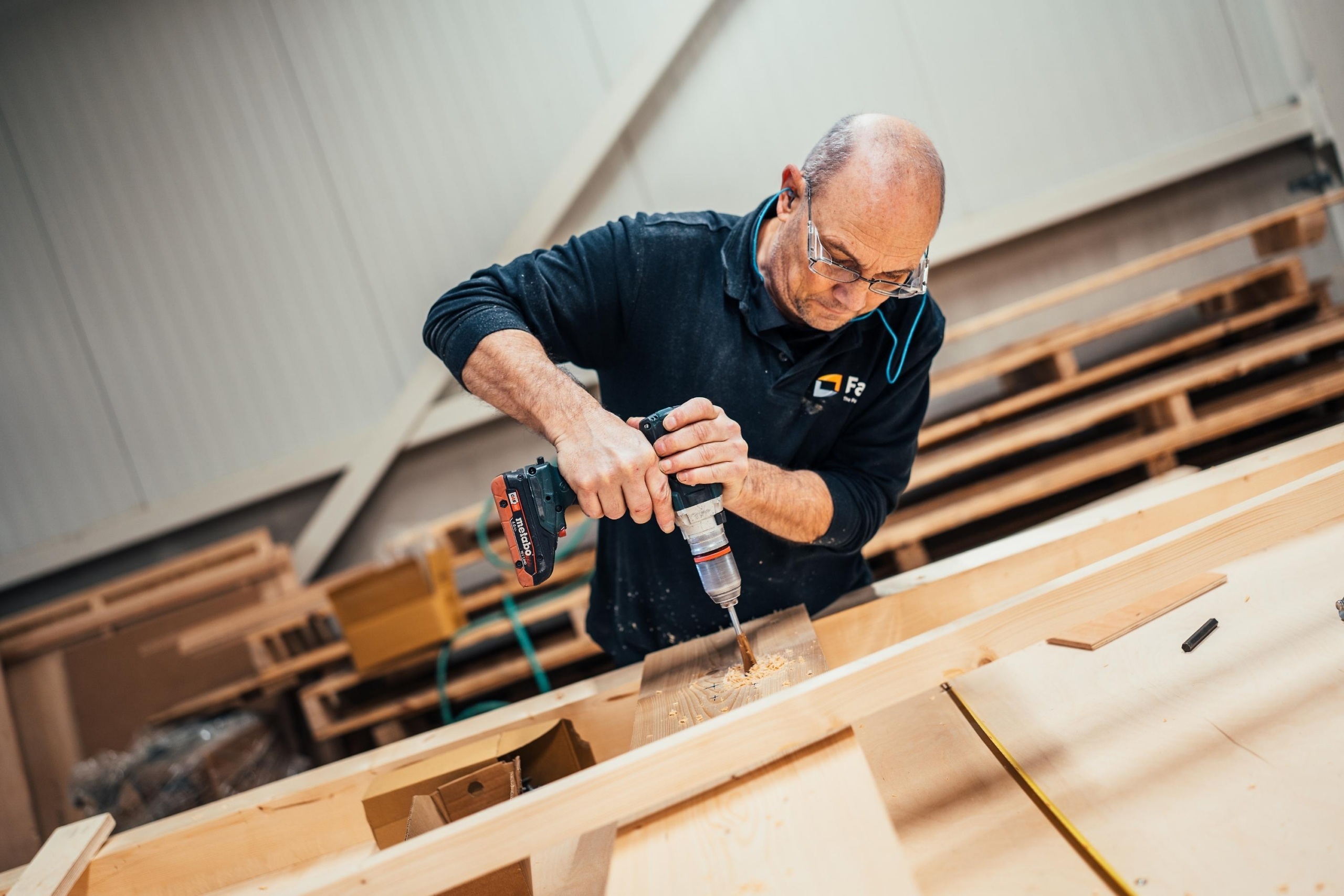 Medewerker van Faes boort een houten onderdeel voor een maatwerkverpakking, waarbij zorgvuldige productie bijdraagt aan het beperken van transportschade en DOA-incidenten.