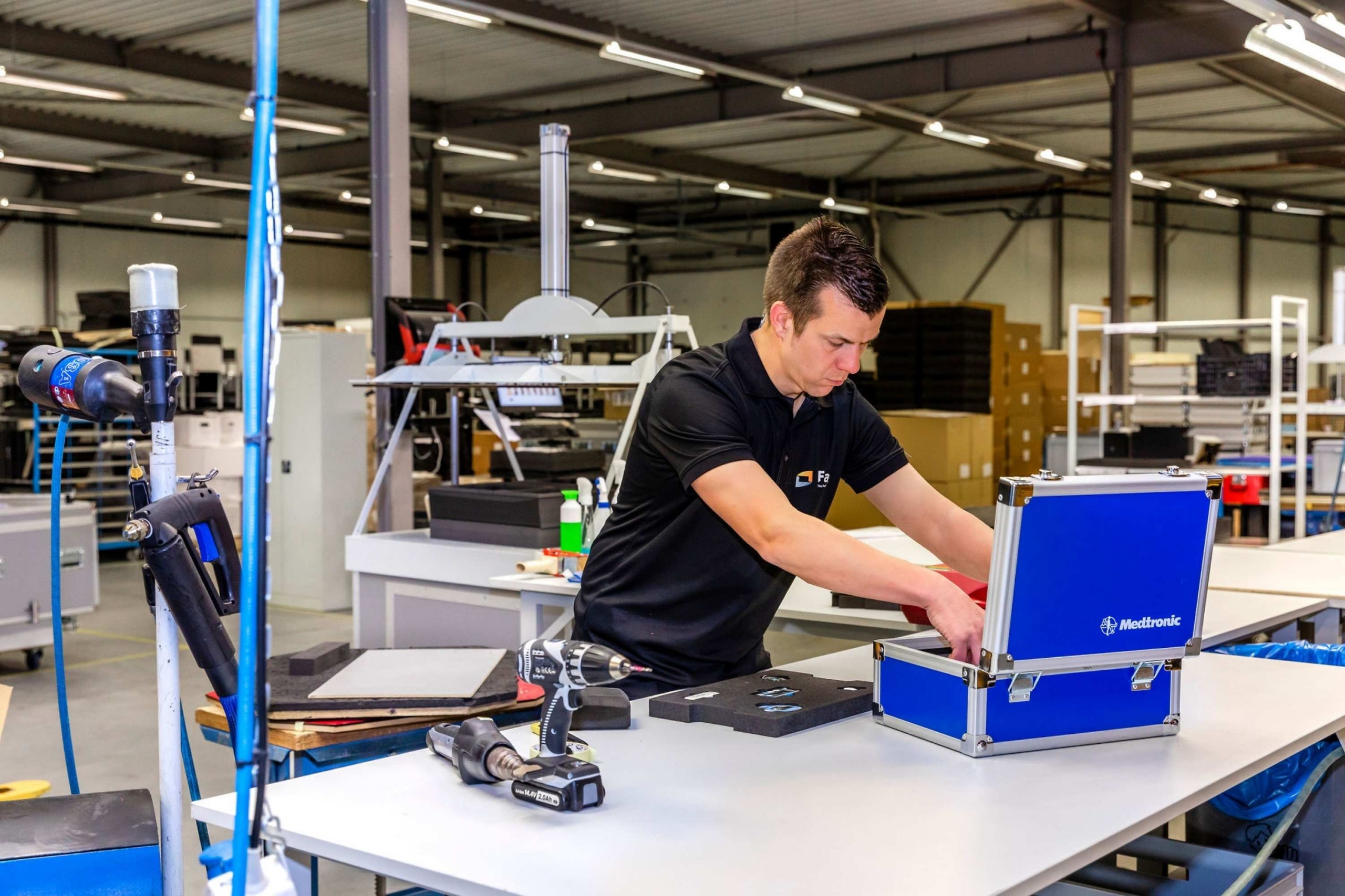 Medewerker van Faes werkt in een productiehal aan een blauwe transportcase op een werktafel, met gereedschap en beschermende inzetstukken naast de case.