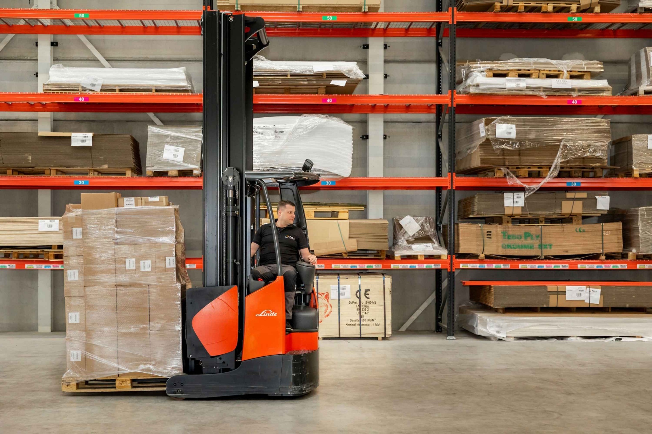 Medewerker van Faes rijdt met een heftruck langs stellingen met verpakkingsonderdelen op pallets, passend bij het zorgvuldig organiseren van transportverpakkingen om DOA-schade te beperken.