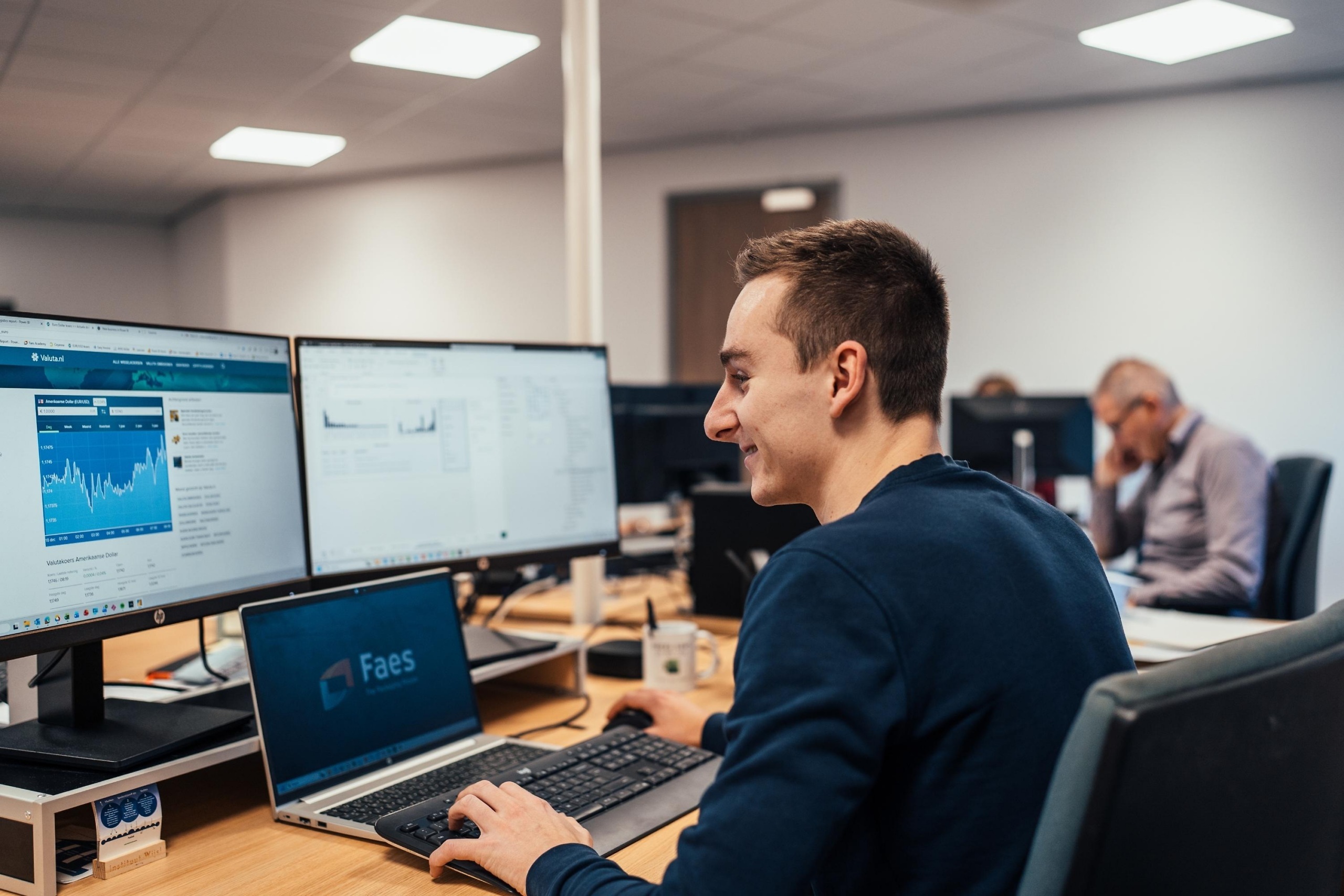 Medewerker van Faes zit op kantoor achter meerdere computerschermen met grafieken en gegevens, passend bij het analyseren van total cost of ownership voor field service equipment.