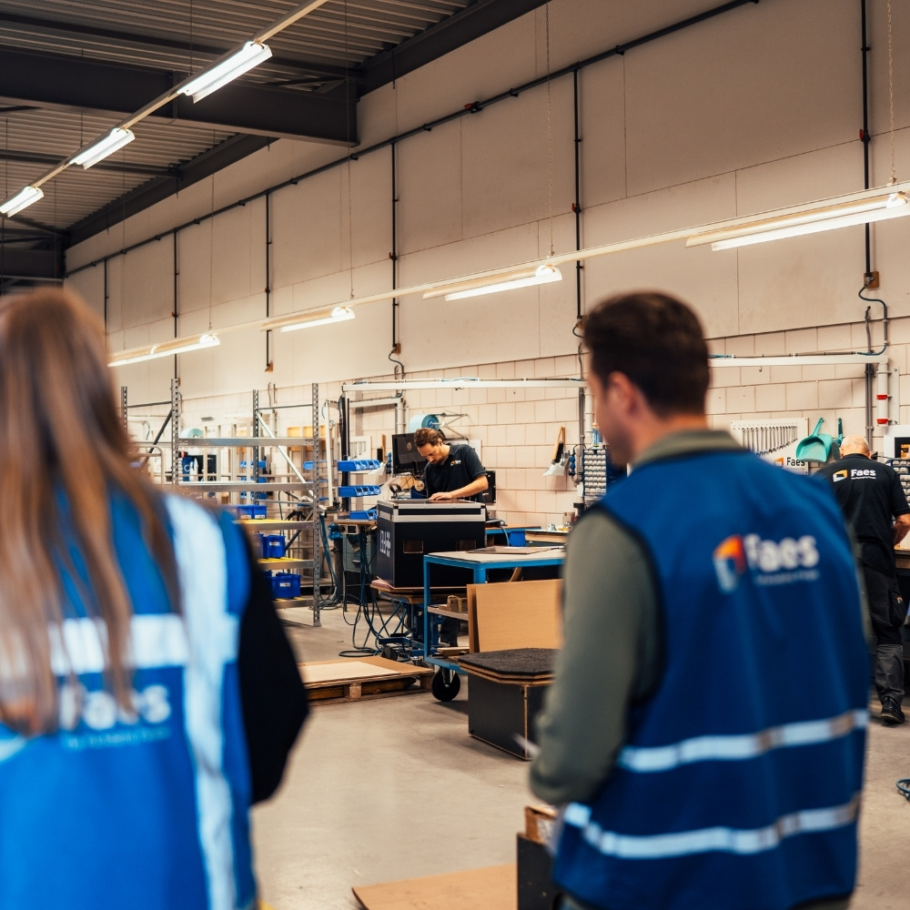 Twee medewerkers van Faes lopen door de productiehal waar beschermende verpakkingen worden samengesteld, als onderdeel van een zorgvuldig proces voor toepassing binnen de ziekenhuislogistiek.