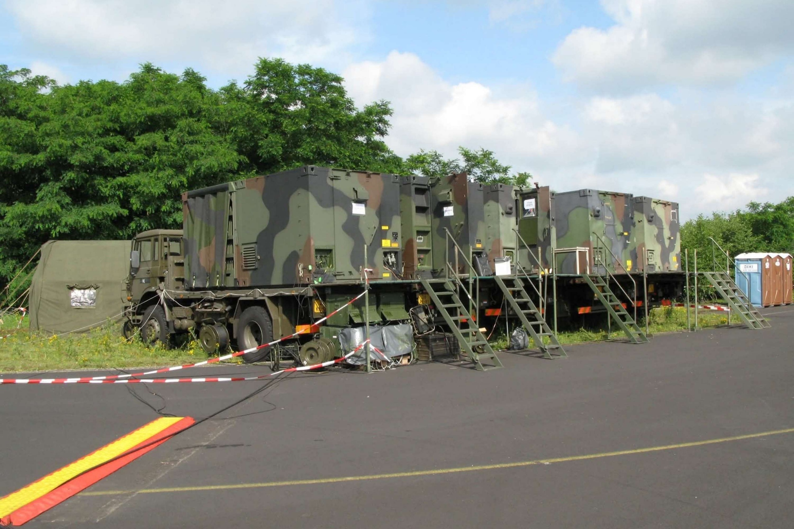 Camouflagekleurige militaire voertuigen staan opgesteld met transportverpakkingen en ondersteunende onderdelen eronder, passend bij de eisen die Faes beschrijft voor militaire transportverpakking.