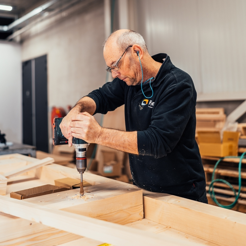 Medewerker van Faes boort in een houten frame in de werkplaats, passend bij zorgvuldige materiaalkeuzes en REACH-compliance binnen industriële verpakkingsoplossingen.