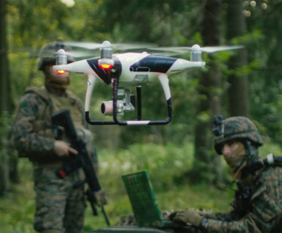Twee militairen in camouflage-uitrusting gebruiken een drone en een laptop voor verkenningsdoeleinden in een bosrijke omgeving.