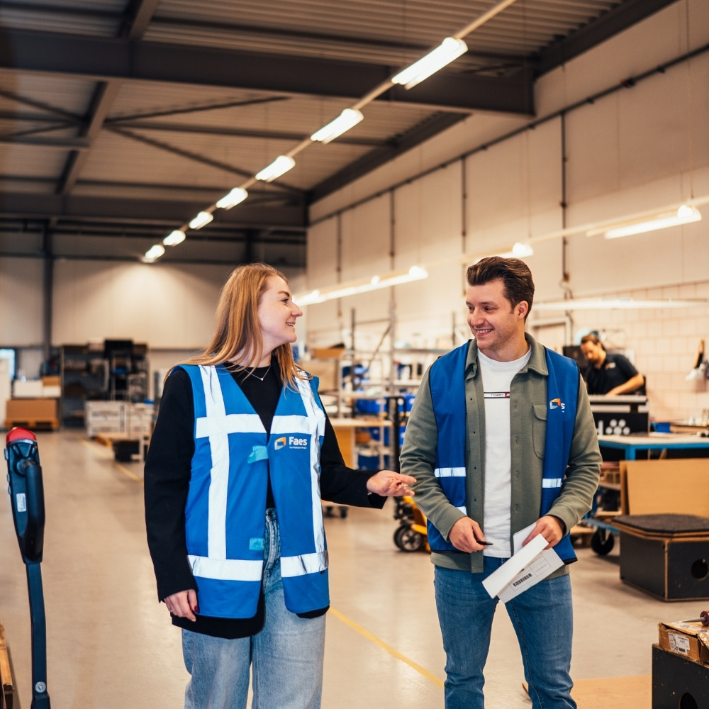 Twee medewerkers van Faes overleggen in de productieomgeving over werkzaamheden rond beschermende verpakkingen en kwaliteitscontrole binnen de supply chain.