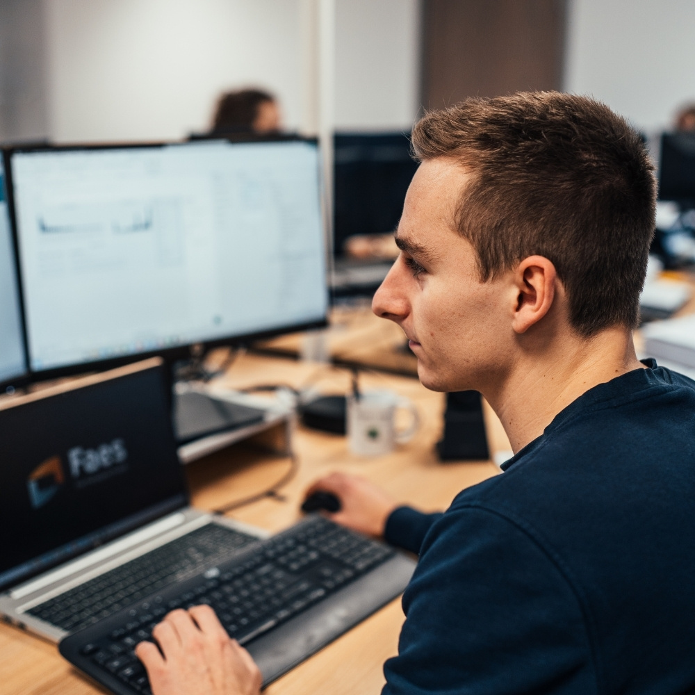 Medewerker van Faes analyseert gegevens op meerdere beeldschermen, passend bij het berekenen en optimaliseren van de totale kosten van verpakkingsoplossingen.