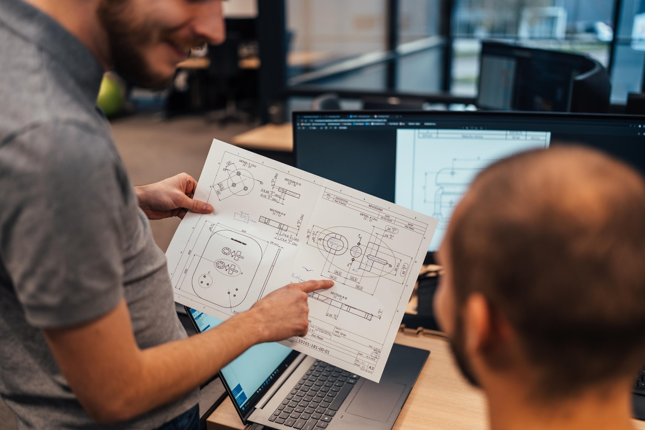 Medewerkers van Faes bespreken aan een bureau een technische tekening, passend bij de zorgvuldige voorbereiding en documentatie die nodig is voor correct lithium batterij transport.