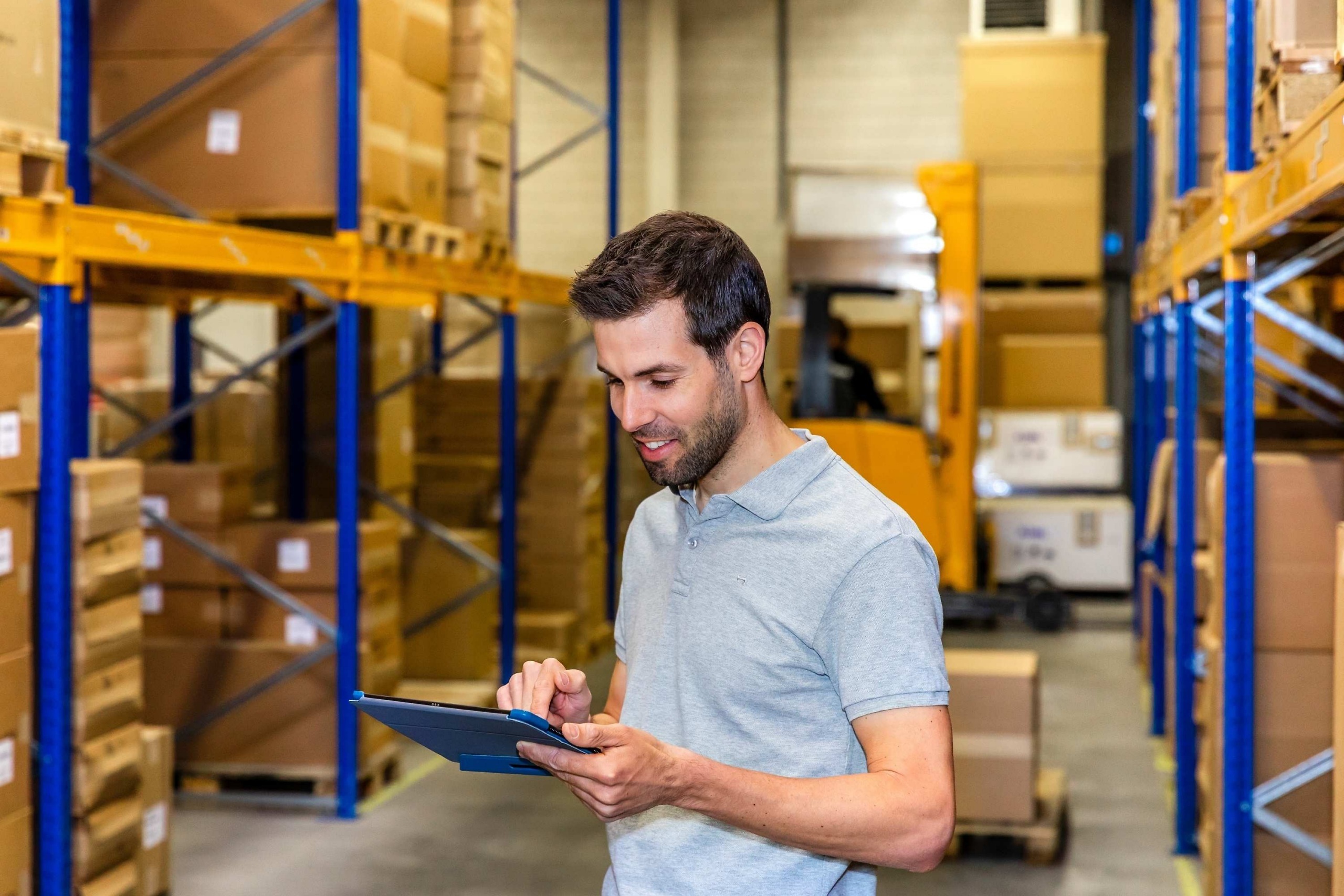 Medewerker van Faes gebruikt een tablet in een magazijn met stellingen en verpakkingsmaterialen, passend bij een artikel over verborgen kosten binnen TCO-modellen en supply chain-processen.
