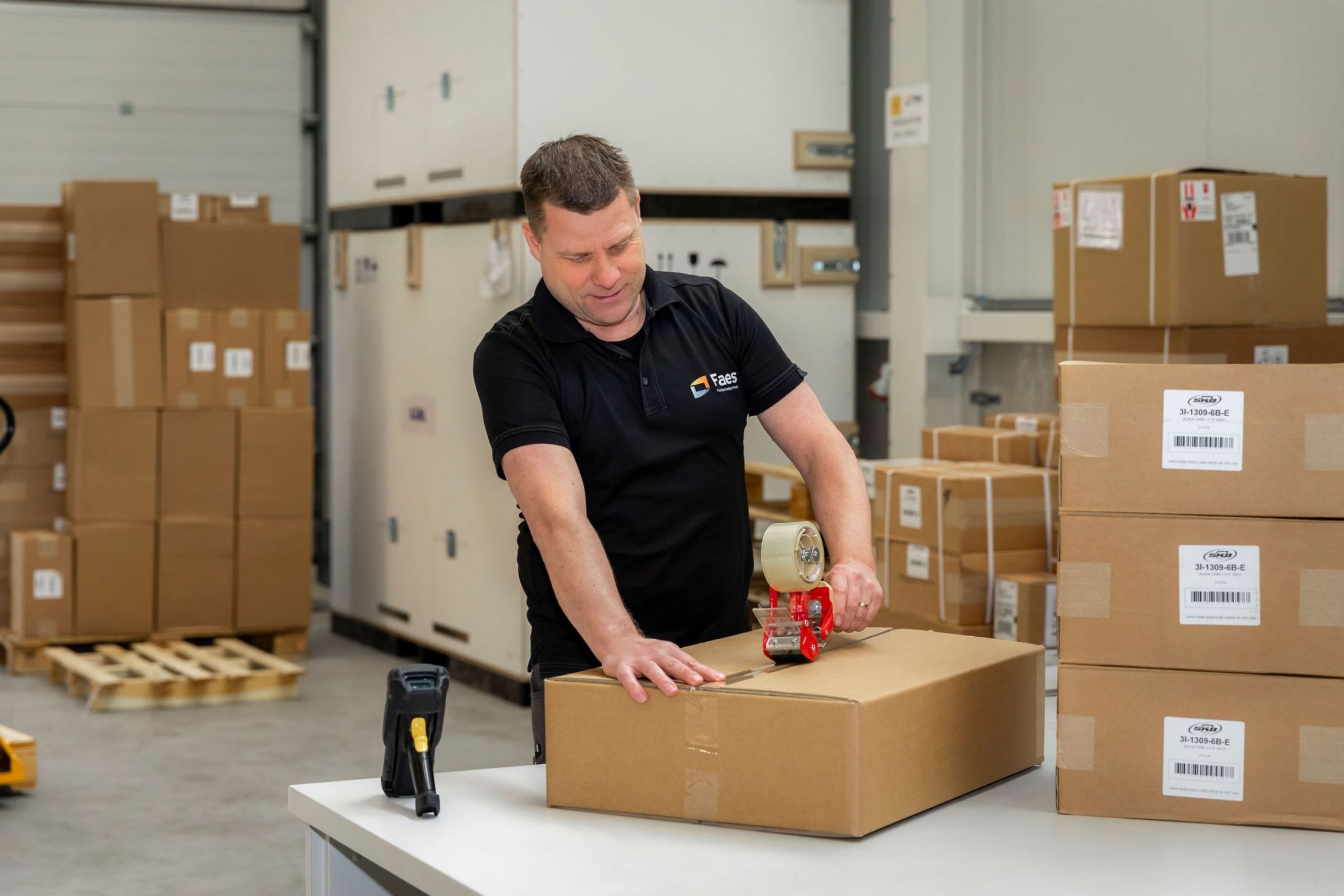 Medewerker van Faes sluit een doos met tape in het magazijn, passend bij het meenemen van verpakkings- en handlingarbeid in de totale kosten van transportverpakking.
