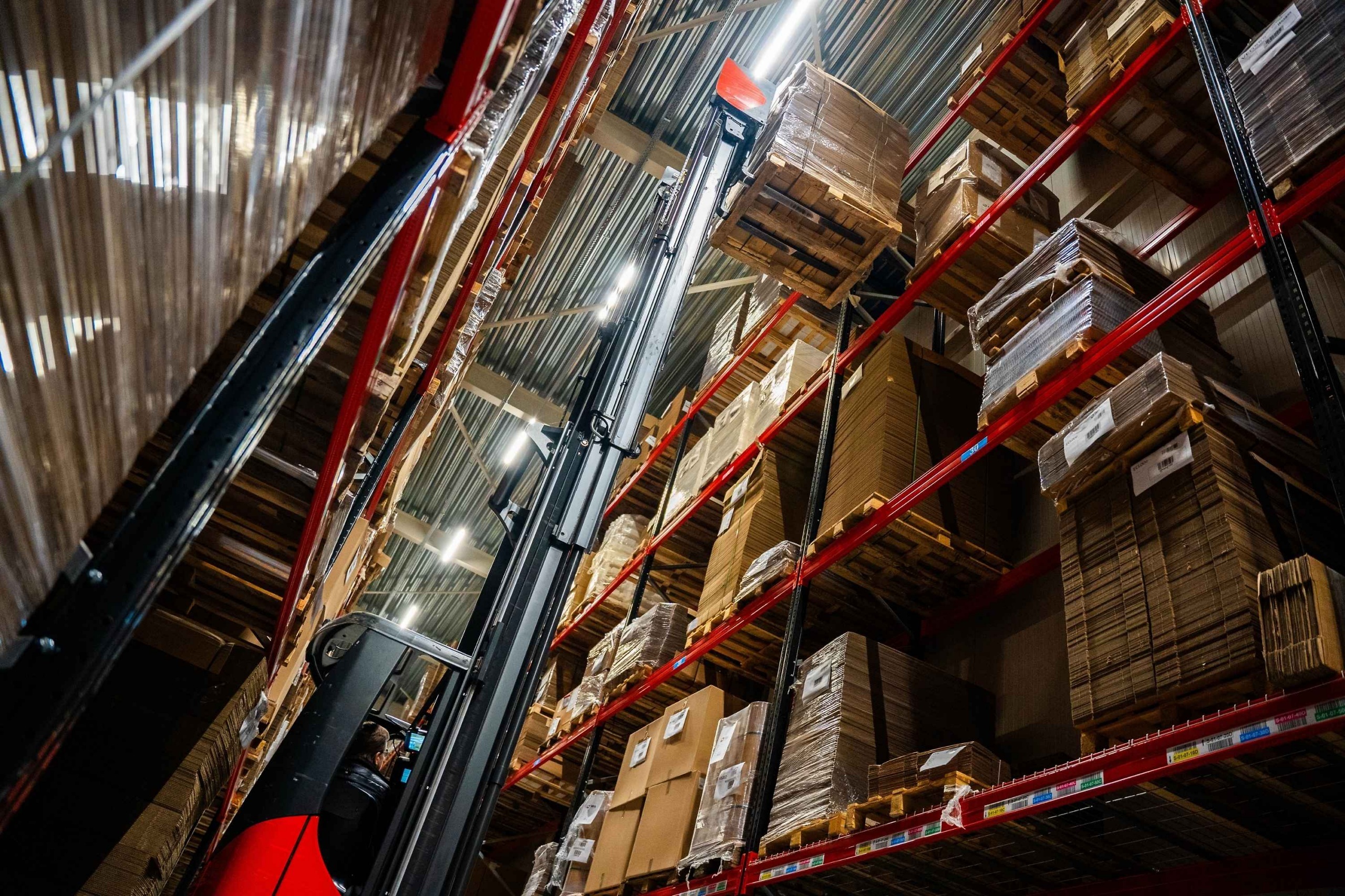 Een heftruck verplaatst bij Faes een pallet tussen hoge magazijnstellingen met verpakkingsmaterialen, passend bij efficiënt voorraadbeheer en het beperken van DOA-risico’s.